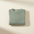 Cozy sage green baby sweater in a warm neutral studio setting